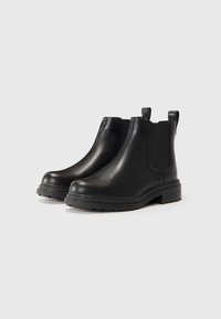 Par de botas Chelsea de cuero negro con paneles laterales elásticos y lengüetas, que cuentan con suelas gruesas con taco para mayor tracción.