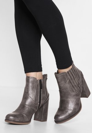 Ankelhøje, mørkegrå læderstøvler med sidelommer og blokhæl båret med sorte leggings på hvid baggrund.