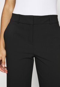 Pantalones negros de tela suave con un corte ajustado. Presentan una cintura plana y bolsillos delanteros. Diseño minimalista, sin patrones visibles.