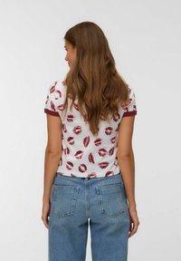 Hvid kortærmet t-shirt med rødt læbeprint, med bordeaux kant rundt om halsudskæringen og ærmerne, parret med blå højtaljede jeans.