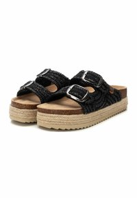 Sandalias negras con tiras trenzadas y dos hebillas ajustables en plata, con plantilla de corcho y una suela intermedia estilo yute tejida sobre una suela de goma texturizada.