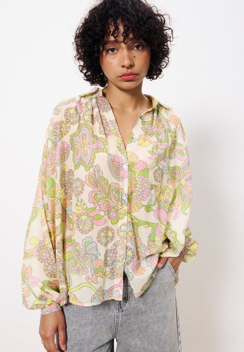 Chemise à manches longues avec boutons, en tissu léger, présentant un motif floral pastel en rose, vert et jaune, avec une coupe décontractée.