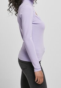 Dlouhý rukáv, rolák v světle levandulové barvě, vyrobený z měkkého materiálu, s přiléhavým střihem a bezšvým designem. Kombinováno s tmavými džíny.