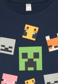 Námořnické bavlněné tričko s pixelovitými obličeji postav z Minecraftu v různých barvách, včetně zelené, růžové a oranžové, v rozptýleném uspořádání.