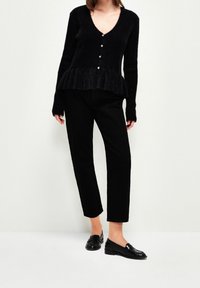 Czarny, puszysty kardigan z długim rękawem, z dekoltem w kształcie litery V i perłowymi guzikami, w zestawie z czarnymi spodniami o prostym kroju i czarnymi mokasynami.