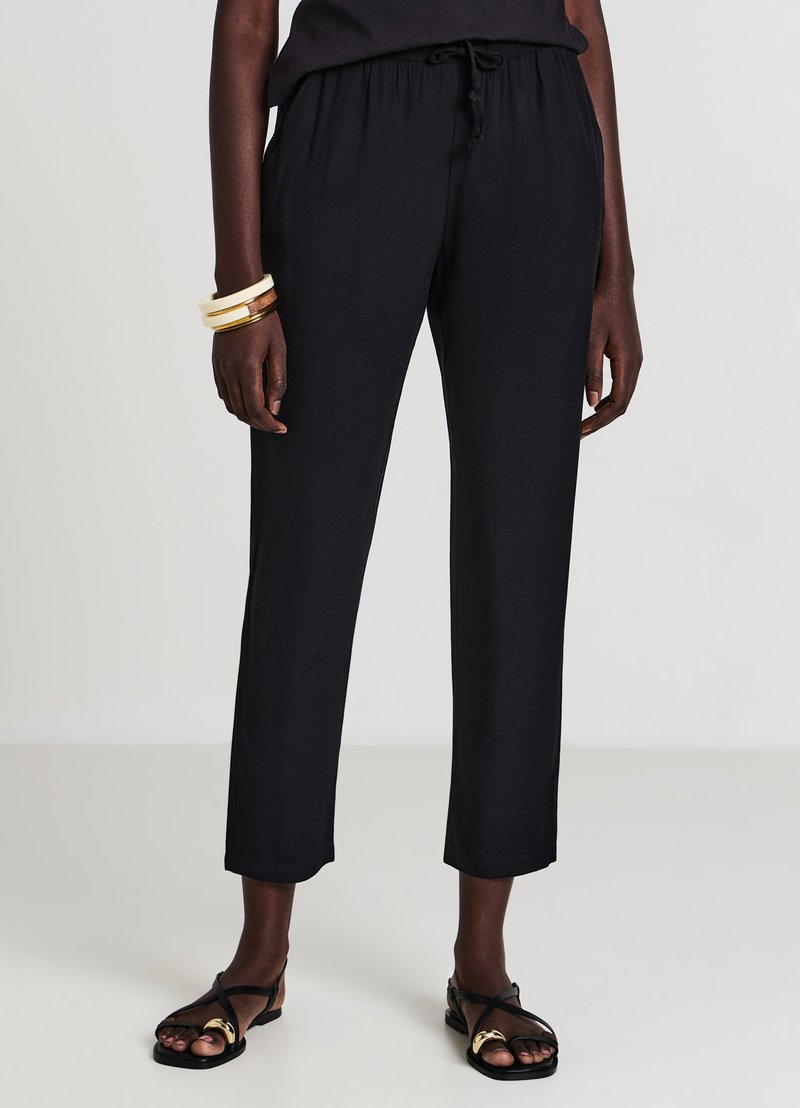 Pantaloni neri leggeri con vestibilità rilassata, vita elastica e coulisse. Caratterizzati da lunghezza corta e texture liscia.