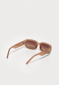 Gafas de sol de tono marrón con montura rectangular, hechas de plástico translúcido, con brazos curvados y un pequeño logo dorado en el lateral.