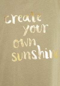 Olivgrüner Stoff mit weicher Textur, der metallic-goldene Schriftzüge enthält, die "Erschaffe dein eigenes Sonnenlicht" in verschiedenen Schriftarten und Stilen anzeigen.