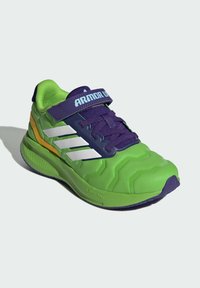 Green athletic shoe with textured surface, purple laces and strap, white stripes, and contrasting yellow accents on the sole and side.