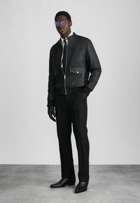 Svart läderbombarjacka med två framfickor, kombinerad med svarta strukturerade byxor och svarta handskar. Tillbehören inkluderar blue solglasögon.