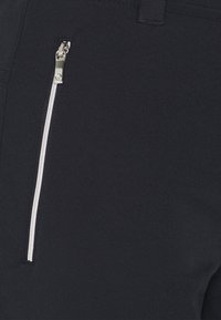 Granatowe spodnie z ukośną kieszenią na zamek błyskawiczny w kolorze srebrnym. Materiał jest gładki, a krój dopasowany z minimalną ilością szwów.