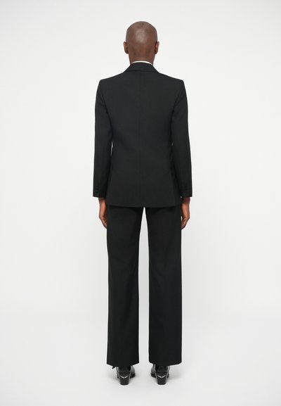 Costume noir ajusté avec un blazer cintré et un pantalon à jambes larges. Tissu lisse, design minimaliste, sans motifs ni embellissements visibles.