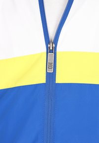 Jachetă colorată cu fermoar, având panouri albe, galbene și albastre; textură netedă; accesorii metalice la fermoar; design athletic.