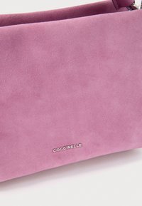 Soft pink suede handbag with small silver COCCINELLE logo and matching strap with gold hardware clasp.