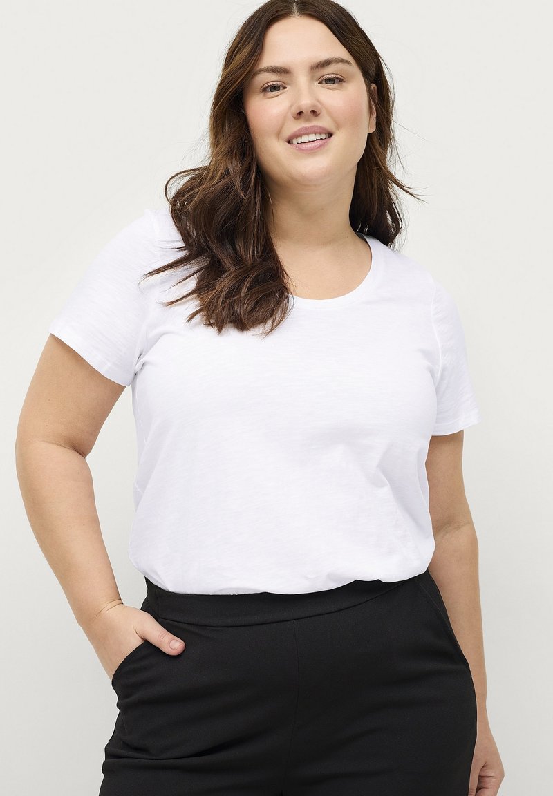 Witte t-shirt met korte mouwen en een ronde hals, gecombineerd met zwarte broek. Het shirt heeft een zachte textuur en een relaxte pasvorm.