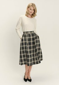 Krémový svetr s jemnými detaily, spárovaný s sukní vzorovanou černobílým kostkovaným motivem do délky ke kolenům, se bočními kapsami a sklady. Černé podpatky.