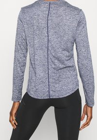 Dlouhý rukáv top v námořnické barevné heather tkanině, s centrálním švem a zaobleným lemem, doplněný černými legínami. Hladká textura.