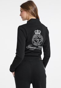 Felpa nera con maniche lunghe, caratterizzata da un grande logo bianco sul retro, realizzata in tessuto morbido con un design aderente e orlo elastico.