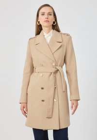 Beige dvouřadý kabát vyrobený z vlněné směsi, s páskem v pase, ramenními epauletami a zlatými knoflíky, s přiléhavým střihem.