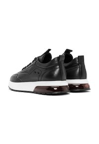 Sneaker nere in pelle con suola bianca, dotate di un accento marrone lucido sul tallone e una finitura testurizzata con delicati dettagli di cucitura.