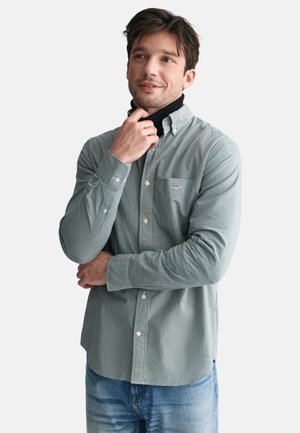Grün-weiß kariertes Button-Up-Hemd mit langen Ärmeln, einer frontalen Tasche und Kragen, kombiniert mit blauen Jeans.