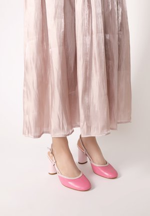 Różowe skórzane buty na obcasie typu slingback z okrągłym noskiem, białym wykończeniem i różowymi słupkowymi obcasami, w zestawieniu z lejącą, jasnoróżową spódnicą.