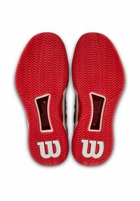 Suelas de goma roja con una textura ondulada, con logotipos blancos en forma de "W" y un área de acento negra con la marca "Wilson".
