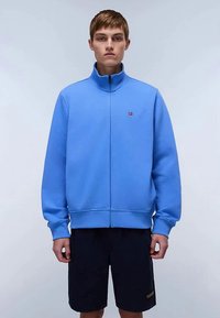 Ανοιχτό μπλε φούτερ με φερμουάρ από βαμβακερό μείγμα. Ψηλός γιακάς, ριμπ μανσέτες και ζώνη στη μέση. Διαθέτει μικρό, κεντημένο λογότυπο στο στήθος.