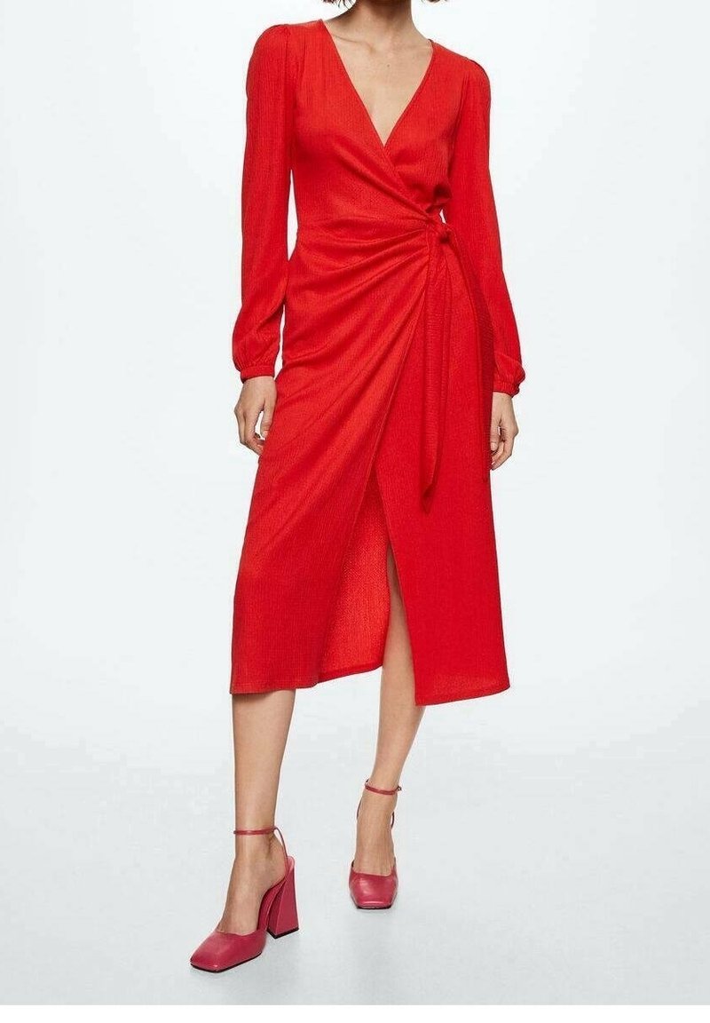 Femme portant une robe portefeuille rouge à manches longues avec un nœud sur le côté et des chaussures à talons blocs à bride cheville assorties, debout sur fond blanc.