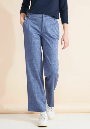 Pantaloni a gamba larga blu chiaro in tessuto texturizzato, con due bottoni in vita e tasche laterali, indossati con scarpe da ginnastica bianche.
