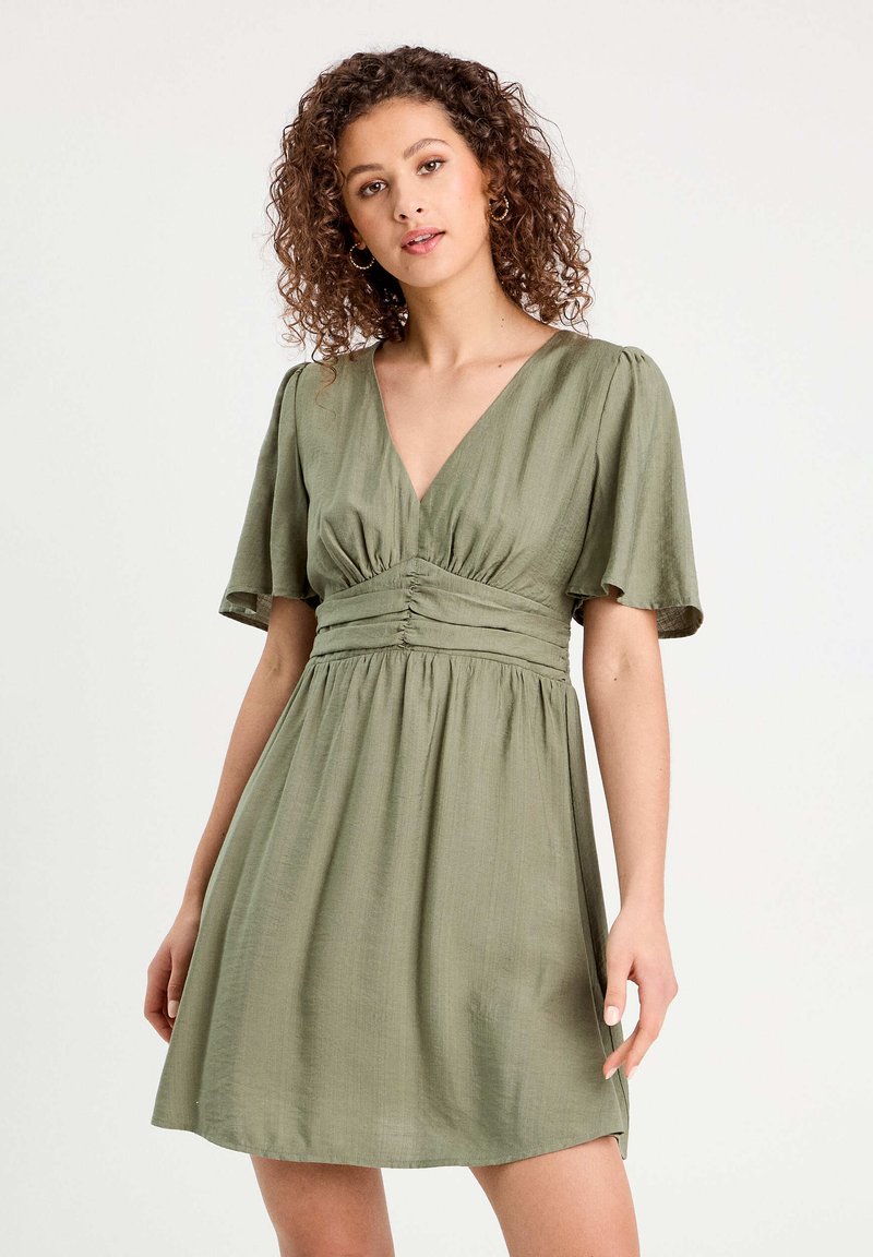 Robe vert olive en tissu doux, dotée d'un décolleté en V profond, de manches courtes à volants, d'une taille froncée et d'une coupe décontractée.