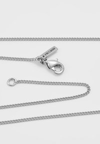 Collana in argento con chiusura a girello e un'etichetta incisa "PILGRIM," caratterizzata da un design piatto con link intrecciati.