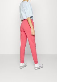 Světlomodré tričko, růžové tepláky, elastický pas, boční kapsy, žebrované manžety, v kombinaci s bílými teniskami. Čistý, pohodlný vzhled zezadu.