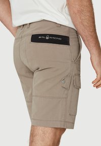 Pantalones cortos cargo beige con bolsillos laterales y un parche en la parte posterior. Fabricados con un material resistente, con detalles de costura y broches de presión plateados.