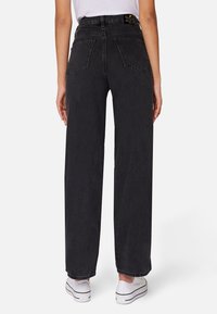 Černé džíny s vysokým pasem a širokými nohavicemi, dvěma zadními kapsami a surovým lemem, doplněné bílými teniskami.