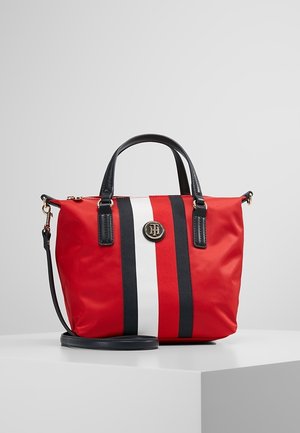 Czerwona torebka z czarno-białymi pionowymi paskami, czarnymi uchwytami, odpinanym paskiem na ramię i okrągłym metalowym logo na środku przodu.
