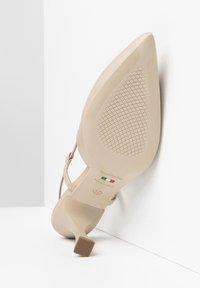 Scarpa con tacco alto beige, dalla punta appuntita, tacco sottile e suola texturizzata. Presenta un'etichetta del marchio e una marcatura della taglia sulla suola.