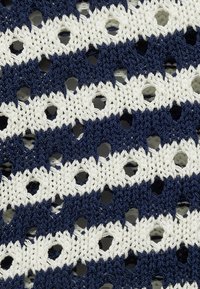 Navy ja smetana heegeldatud kangas, millel on vahelduvad horisontaalsed triibud, märgatavate avatud aukudega ja tekstuurse mustriga.