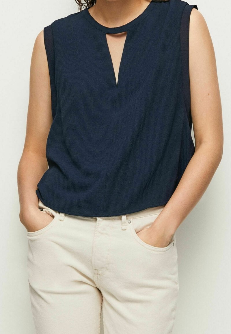 Top senza maniche blu navy con scollatura a chiave e tessuto testurizzato. Abbinato a pantaloni chiari a vestibilità comoda.