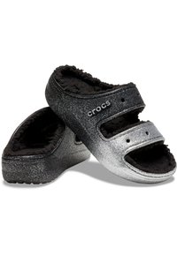 Crocs neri e argento glitterati con due cinturini regolabili e un morbido rivestimento in pelliccia nera. Presenta una suola robusta e una finitura testurizzata.