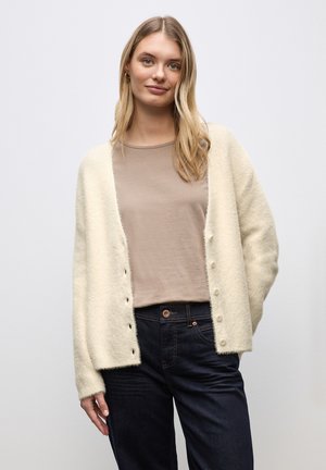 Crème-kleurige cardigan van zacht, textured stof, met een relaxte fit, knopen aan de voorkant en lange mouwen, gedragen over een beige top.