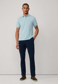 Světle modrá polo košile s krátkým rukávem a límečkem, spárovaná s námořnickými kalhotami a hnědými slip-on botami. Jednoduchý design, hladká textura.