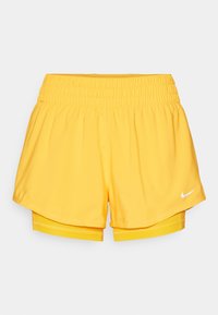 Gelbe Sportshorts mit einem elastischen Bund, die ein geschichtetes Design aufweisen und ein kleines weißes Nike-Logo auf der rechten Seite haben.