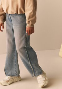Jasnoniebieskie dżinsy z luźnym krojem, z surowymi szwami i delikatnym wyblaknięciem. W zestawie z białymi i beżowymi sneakerami.