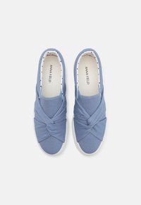 Light blue canvas slip-on shoes featuring a knotted design on the upper, white rubber sole, and polka dot insole lining.