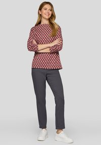 Rosa- und weiß gemustertes Oberteil mit drei Viertelärmeln, kombiniert mit grauen Hosen und weißen Turnschuhen. Textilstruktur, lässige Passform.