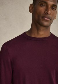 Burgandy crew neck-tröja tillverkad av slätt stickat tyg, med en ribbad krage och mudd, åtsittande design, minimal detaljering.