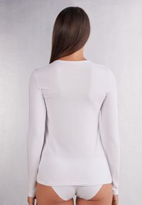 Langärmliges, weißes, figurbetontes Oberteil mit rundem Ausschnitt und glatter Textur, mit geradem Saum und minimalistischem Design.