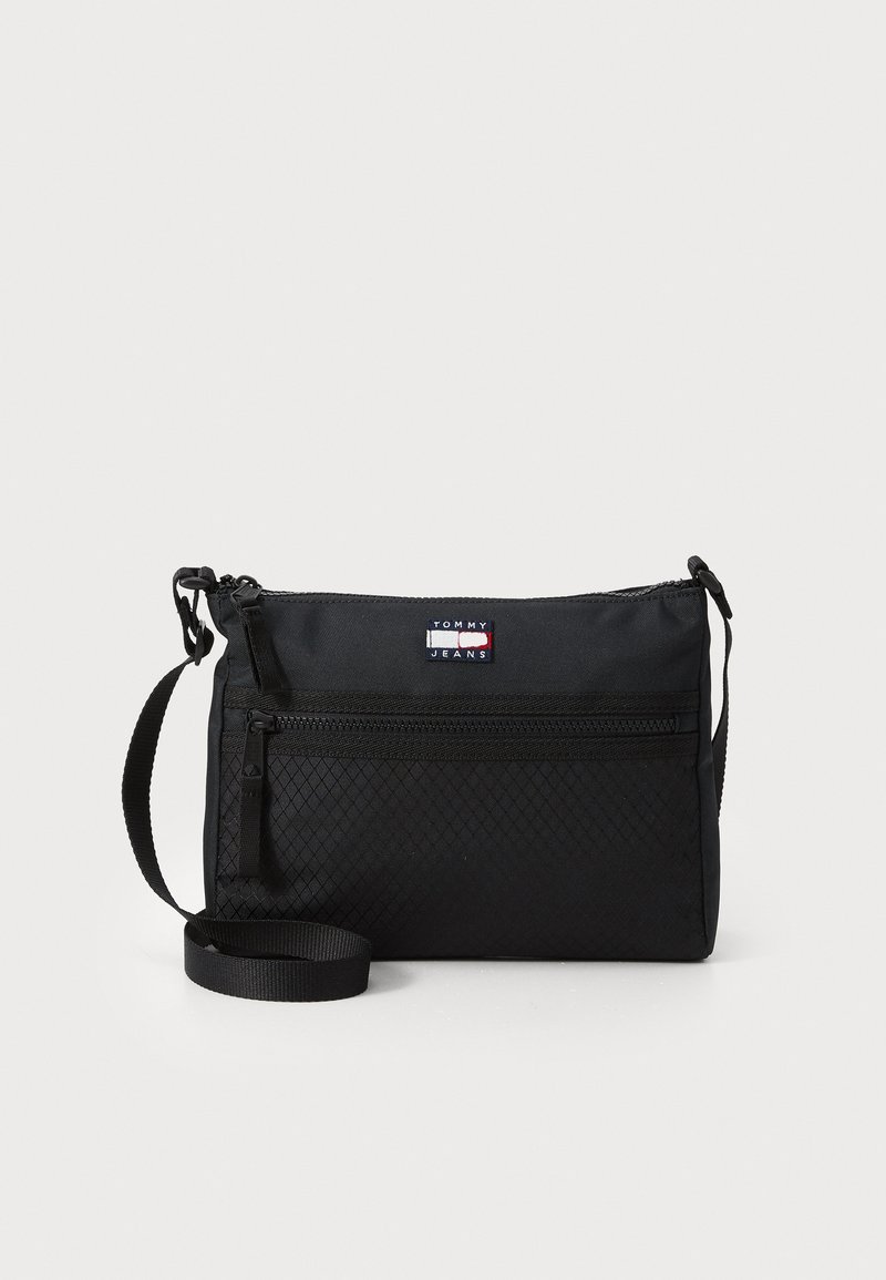 Sac à bandoulière noir en nylon durable avec un motif texturé. Dispose d'une poche zippée à l'avant et d'une sangle réglable. Logo Tommy Jeans visible.