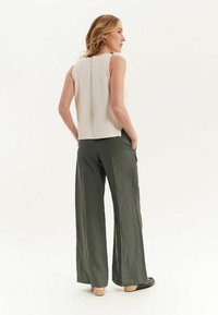 Haut sans manches de couleur beige clair et texturé, associé à un pantalon large et loose de couleur olive. Le mannequin est de dos, montrant la coupe décontractée et les tons neutres.